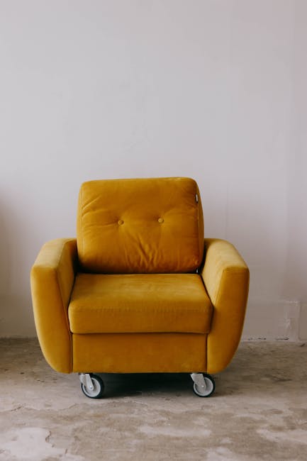 A clean, upholstered cream sofa with button-tufted backrest and rolled armrests is positioned against a white wall with decorative paneling. The sofa is situated on a wooden floor, and the room is wel